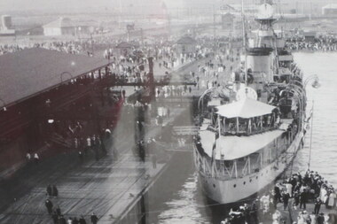 Black & white photo of a ship docked at a wharf, crowds of people are also on the pier.