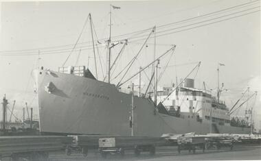 Photo of the cargo ship "Wangaratta" berthed on the Yarra River.  The rail carts shown in front of the ship are loaded with timber.