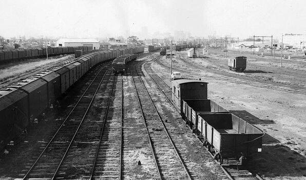 Photo shows the Port Melbourne railway yards, 1969. Several types of cargo trains are shown and in the distance you can see the Melbourne skyline.