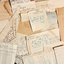 A close up view of an unorganised pile of notes and letters of varying sizes. Some are small scraps of paper, some are envelopes and some are full letters. Most of the details are handwritten but one of the letters is typed.