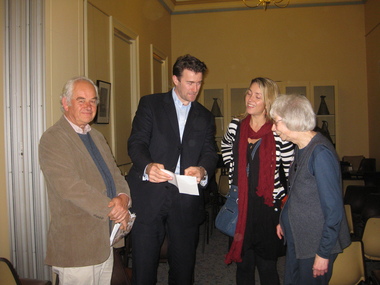 A man shows a piece of paper to two women on his left. A man on his right is looking at the camera smiling.