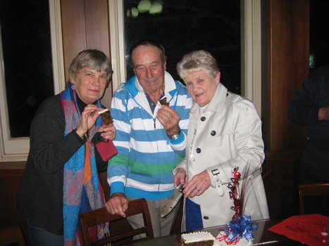 A man and women display their slices of cake for the camera. A third person, a women, holds a large knife with the remaining portion of the cake on the table in front of her.