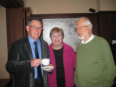 A man, with a cup and saucer, women and another man pose for the camera.