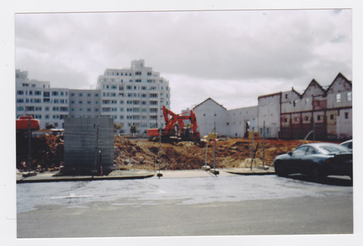 Demolition site of a large building, photo shows digger at work with a security wire fence at the front of the site. 