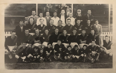 Black & white photograph of a football team, some are in their football gear, whilst others are dressed in suits or training gear.