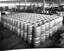 Interior of a factory showing over 100 metal barrels stacked two high.