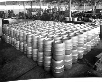 Interior of a factory showing over 100 metal barrels stacked two high.
