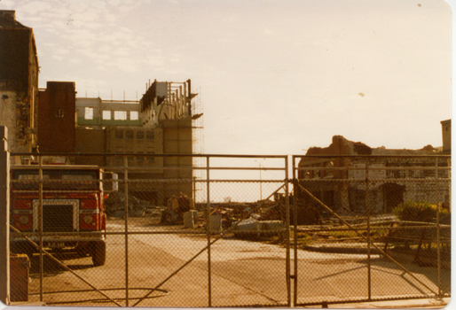 Partially demolished factory buildings behind cyclone wire gates.