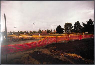 Looking from vacant land within an orange temporary fence over more vacant land towards established houses.