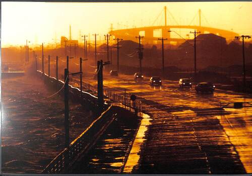 Waves breaking on the seafront sending spray over the road at sunset.