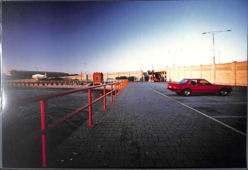 A carpark with a red car next to the see and beside two road ramps that meet at right angles.