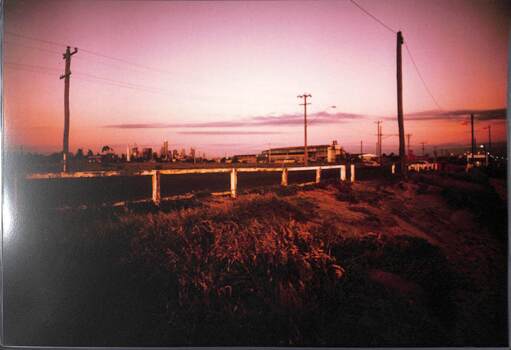 View towards the city skyline in the very far distance over a road with a simple white fence.