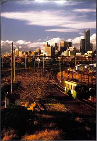 View from a raised position of a tram travelling towards us with the city skyline in the background.