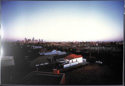 View from a raised position over the rooftops towards the city skyline. "Not for Sale" is painted on the roof of one of the houses.