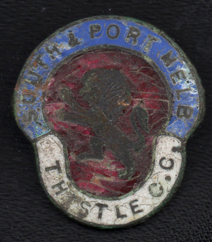 Badly scuffed badge with 'SOUTH & PORT MELB' in a blue band around the outside of the wider top section and 'THISTLE C.C.' in a white band around the lower section. The centre red section has a heraldic lion.
