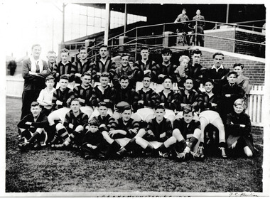 Group of men posing in three rows in typical football team formation in front of an empty grandstand.