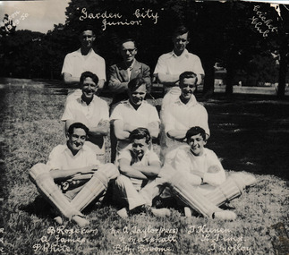 Eight men/boys in cricket whites and one man in street clothes posing the three rows. Names written at bottom of the photo.