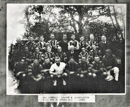 A group of men posing in three rows in football team formation. Most are wearing striped football uniforms, one appears to be wearing an umpire's whites while another is a trainer. Three men are wearing street clothes.