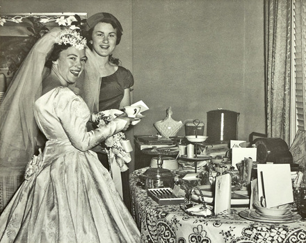Bride and bridesmaid standing next to a table covered with gifts.
