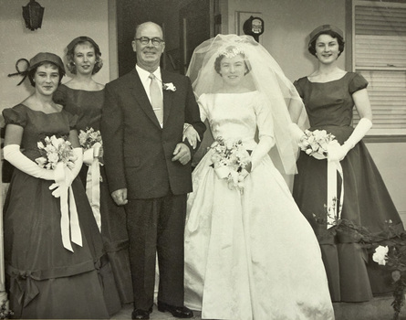 A bride and three bridesmaids pose outside a house with a man in a suit.