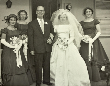 A bride and three bridesmaids pose outside a house with a man in a suit.