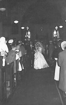 A bride and groom walk down the aisle of a church with people standing in the rows of pews on either side