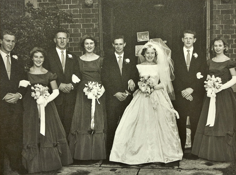 A bride and three bridesmaids pose with four men in suits