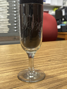 Clear glass with a short stem and SBC engraved on the flute-style bowl