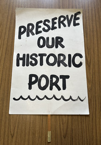 White cardboard placard attached to a wooden handle with black hand-printed slogan - Preserve Our Historic Port