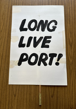 White cardboard placard attached to a wooden handle with black hand-printed slogan - Long Live Port!