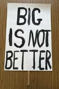 White cardboard placard attached to a wooden handle with black hand-printed slogan - Big Is Not Better
