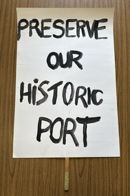 White cardboard placard attached to a wooden handle with black hand-printed slogan - Preserve Our Historic Port