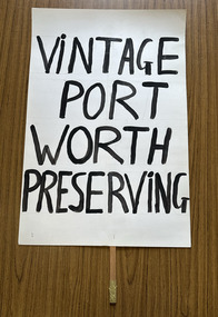 White cardboard placard attached to a wooden handle with black hand-printed slogan - Vintage Port Worth Preserving