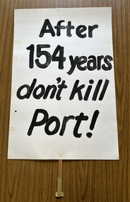 White cardboard placard attached to a wooden handle with black hand-printed slogan - After 154 years don't kill Port!