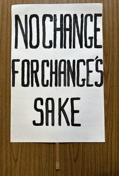 White cardboard placard attached to a wooden handle with black hand-printed slogan - No Change for Change's Sake