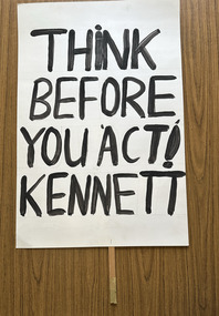 White cardboard placard attached to a wooden handle with black hand-printed slogan - Think Before You Act! Kennett
