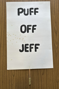 White cardboard placard attached to a wooden handle with black hand-printed slogan - Puff Off Jeff