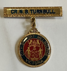Round gold-coloured badge with red and blue enamel with a coat of arms and "City of Port Melbourne Victoria" written around the outside suspended from a gold-coloured bar with the inscription "Cr. N. S. Turnbull". 