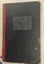 Book has black hardboard cover with red spine and worn edges.