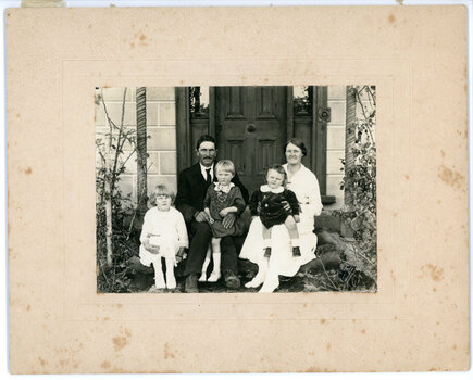 Family of two adults and three children sitting on front of the door of a house
