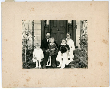 Family of two adults and three children sitting on front of the door of a house