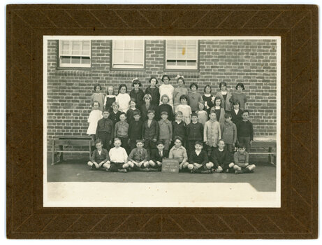 Children posing for a school photo. The photograph has been taken in front of a brick wall with three windows.