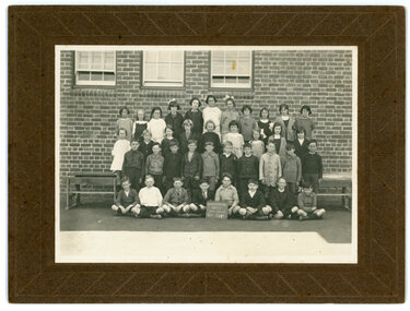 Children posing for a school photo. The photograph has been taken in front of a brick wall with three windows.