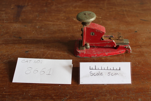small red metal stapler with large round button on top
