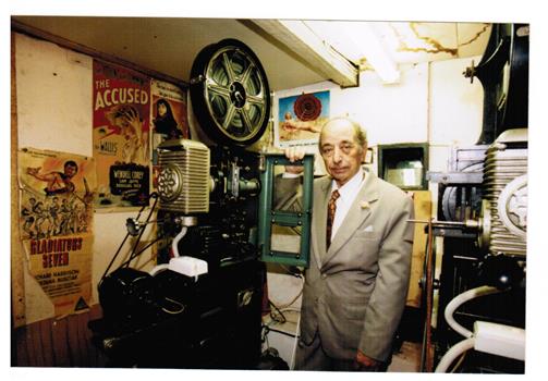 A man standing beside a fim projector.