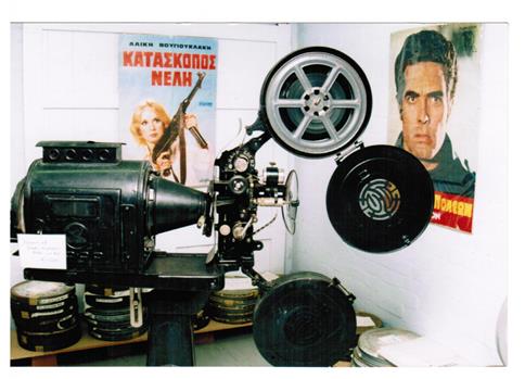 A film projector and film reels and posters in Greek on the wall.