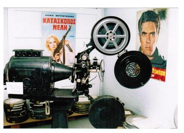 A film projector and film reels and posters in Greek on the wall.