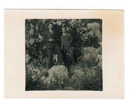 Two men standing in front of shrubbery.