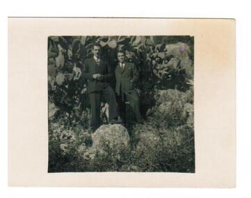 Two men standing in front of shrubbery.
