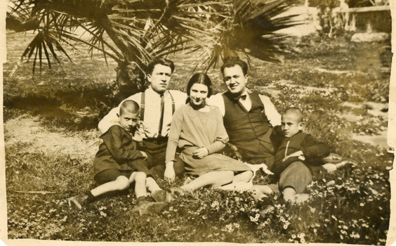 Photograph of two men, two boys and a girl sitting under a tree.